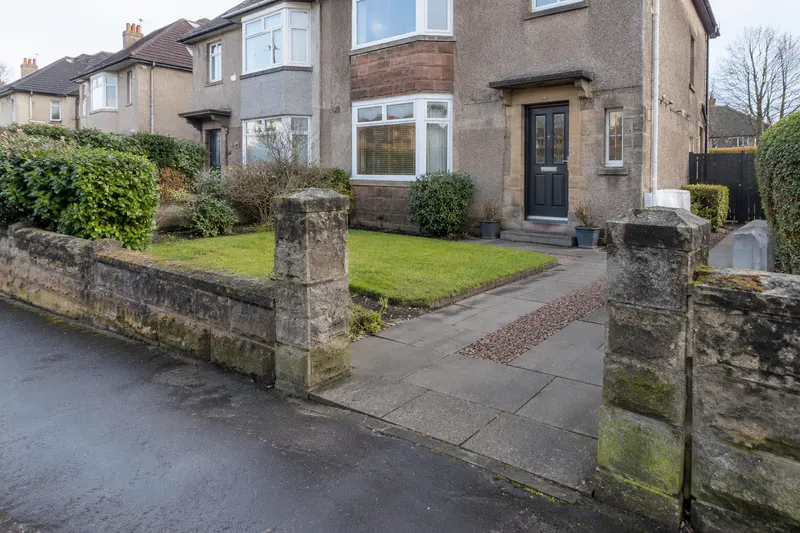 Low sandstone wall framing a driveway entrance and retained front lawn