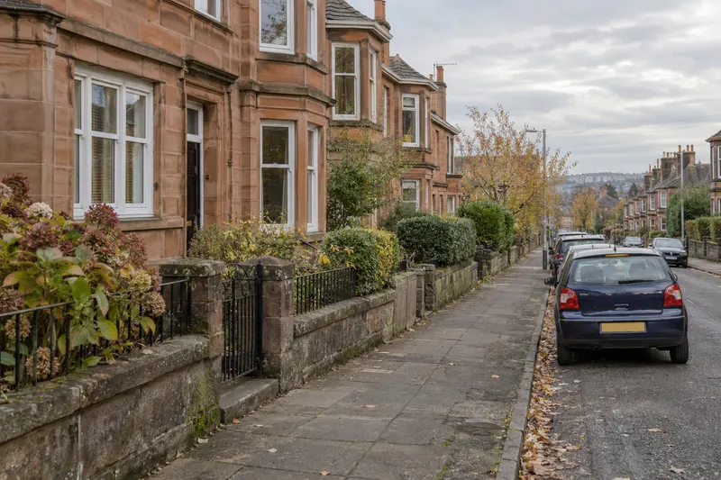 Clear pavement beside sandstone houses with a car parked wholly on the road