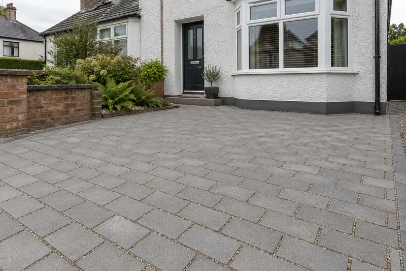 Grey driveway paving with stone-filled joints and a planted border